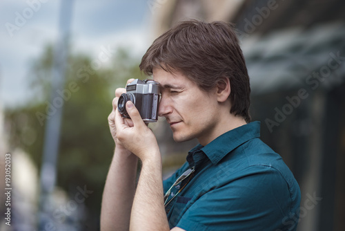 Young attractive man, a photographer, taking photographs in an urban area with an analog SLR camera