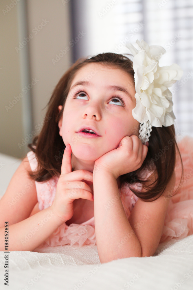 Naklejka premium 6 or 7 Years Old Little girl with Dark Hair and Brown Eyes, with White Flower Headband,Funny Expression, dreaming, happy posing isolated on blurry background