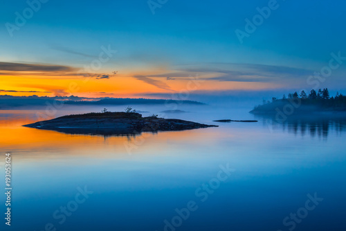 Fog over Lake. Sunrise in the fog. Wild nature of Finland. Islands of stone. Mirror reflection in water. Summer in Finland.