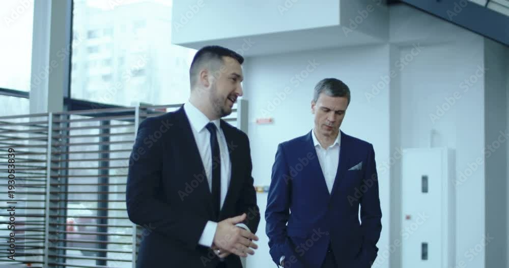 Slow motion of adult agent in suit talking to customer and walking to new car in showroom. Slow motion of adult agent in suit talking to customer and walking to new car in showroom.