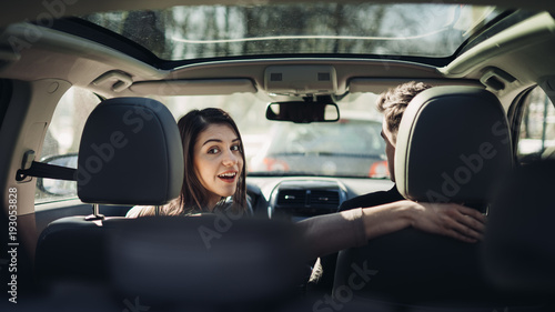 Young woman in a car,female driver looking at the passenger and smiling.Enjoying the ride,traveling,road trip concept.Driver feeling happy and safe.Learning how to drive,getting drivers licence. © eldarnurkovic
