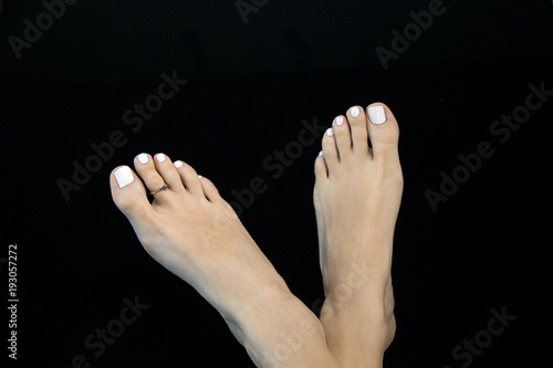 Isolated beautiful feet close up, woman bare feet with smooth skin, white manicure, well cared, soft, with ideal Greek foot toe, black background