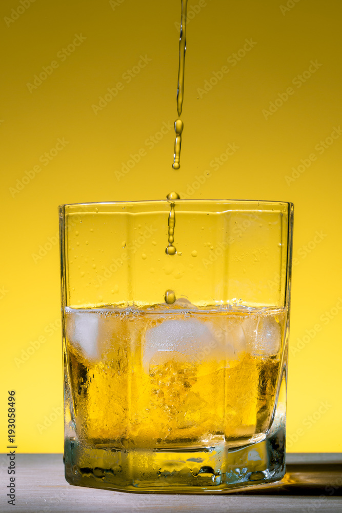 Whiskey being served in a glass with ice on a yellow background Whiskey being served in a glass with ice on a yellow background