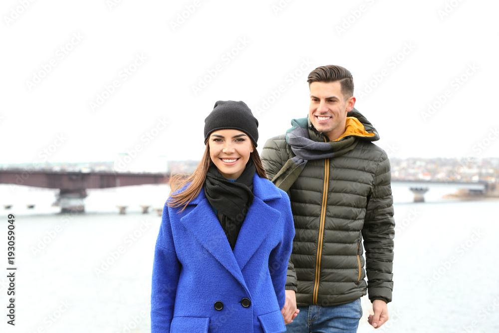 Beautiful couple in warm clothes walking near river