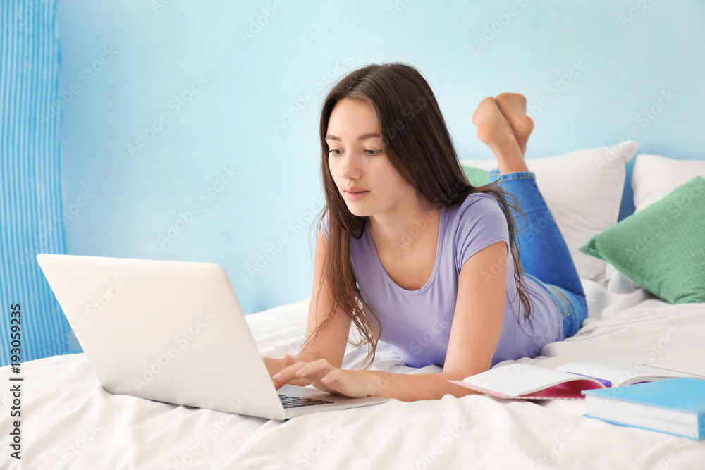 Cute teenager girl using laptop while doing homework in bedroom Cute teenager girl using laptop while doing homework in bedroom