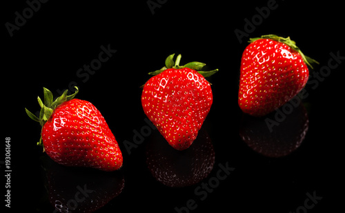 three ripe berry red strawberry on a black polished background.