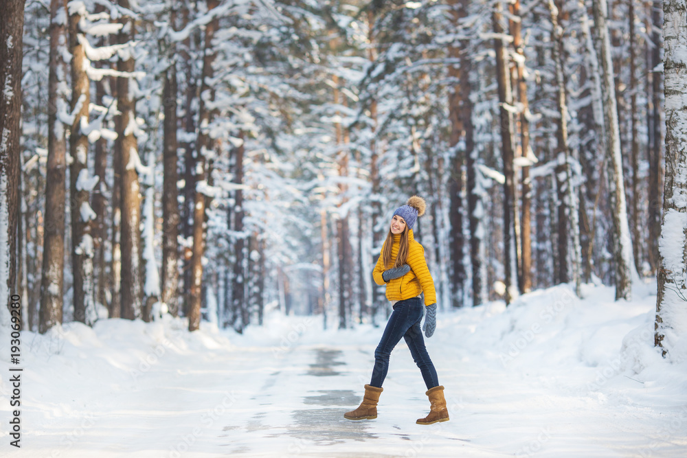 Young pretty woman in a bright clothes walks on a road in a winter forest