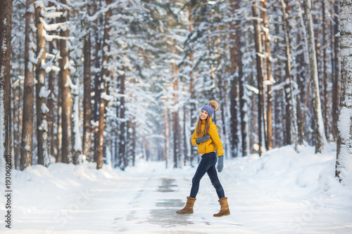 Young pretty woman in a bright clothes walks on a road in a winter forest