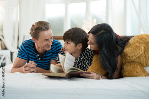 Dad and mom looking at my son reading a book is on the bed in the family education ideas.