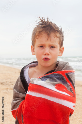 The child is wrapped in a blanket in cool weather on a deserted beach