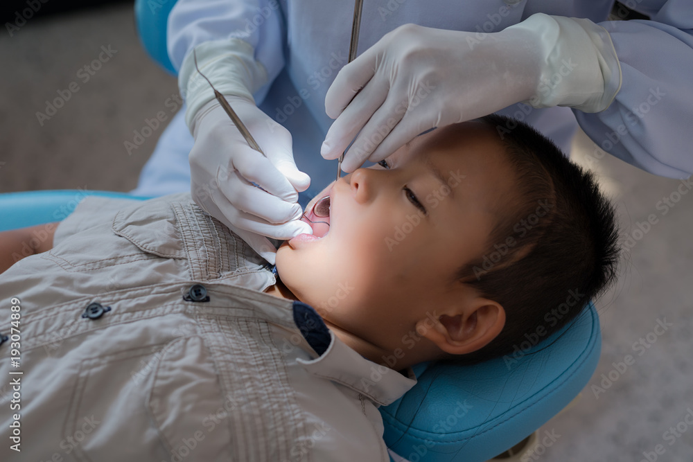 Hands of dentist holding a dental tool. Checking the teeth to the boy lying in the dental chair in a hospital. Hands of dentist holding a dental tool. Checking the teeth to the boy lying in the dental chair in a hospital.