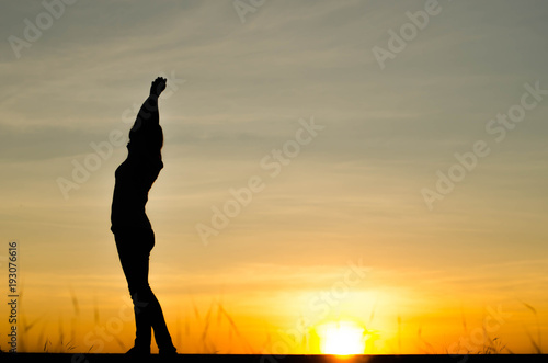 Woman silhouette is standing, raise one's hand for exercise, on evening .