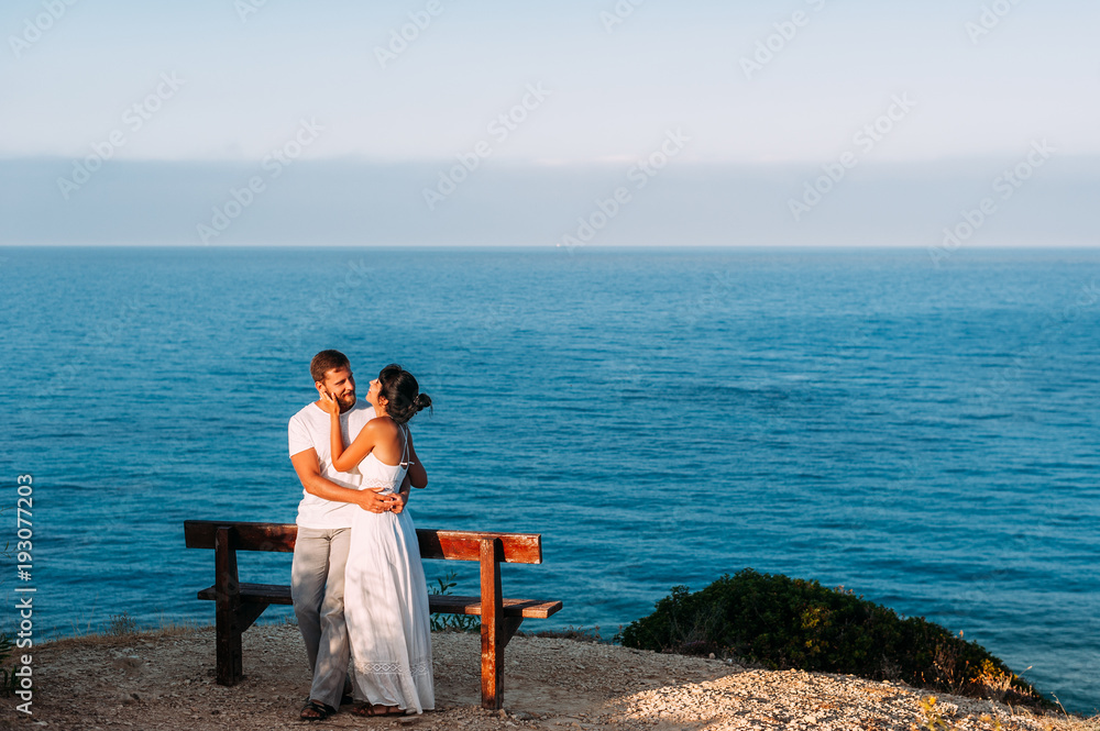 A couple in love meets the sunrise at the sea. Honeymoon. Honeymoon trip. Boy and girl at the sea. Man and woman traveling. Couple hugs. Couple kissing. Newly married couple. Lovers. Holiday romance