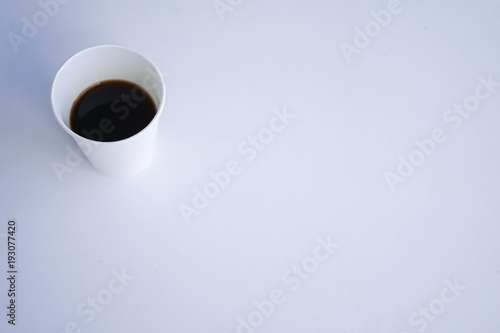Paper (disposable) white cup with coffee close-up. Blurred background. Top view with copy space