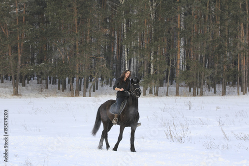 Woman on black horse in snowy forest