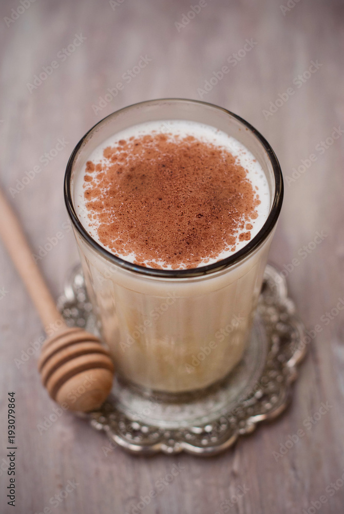 Glass of Milk with Cinnamon or Cocoa Powder with Honney Spoon on rustic background. Healthy Breakfast. Vertical Image.