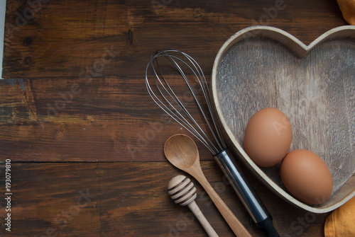 Kitchen Tools for Bakerry or cooking. Raw Eggs with wooden spooon, Orange Napkin, Heart Shape Box and Baking tools. Copy Space. Flat Lay. photo