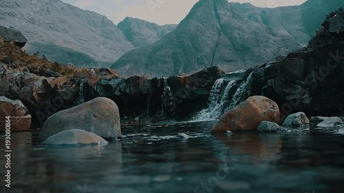 Crystal Clear Water at River with Waterfalls and Looming Mountains