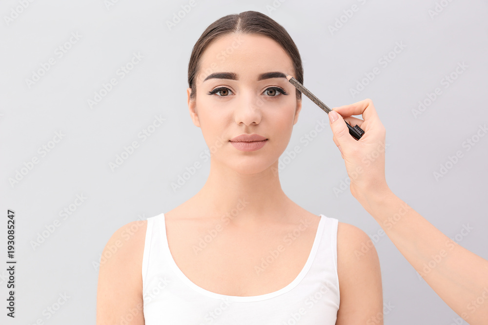 Fototapeta premium Young woman undergoing eyebrow correction procedure on light background