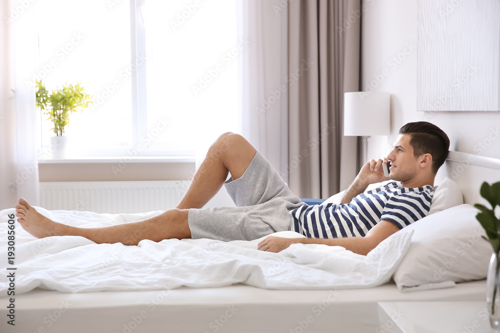 Young handsome man with mobile phone on bed at home Young handsome man with mobile phone on bed at home