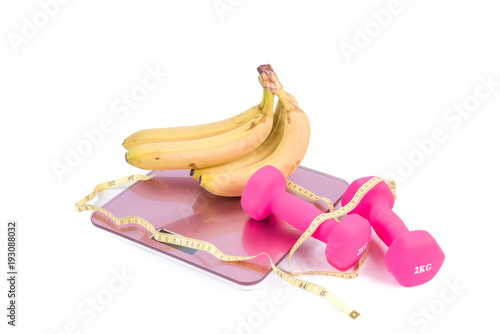 Banana fruits and dumbbells tied with a measuring tape on a weighting scale 