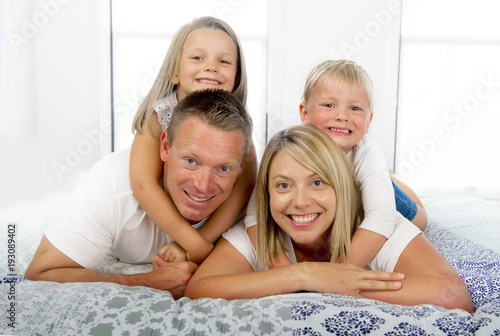 young beautiful and radiant couple 30 to 40 years old smiling happy posing sweet lying on bed with little son and beautiful daughter at home