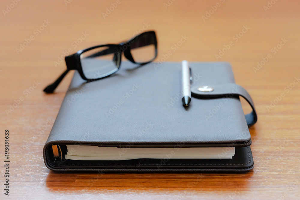 Copy space and selective focus at border of the diary book on the wood / Design composition with pen and glasses on the diary book / concept of study , work and stationary 