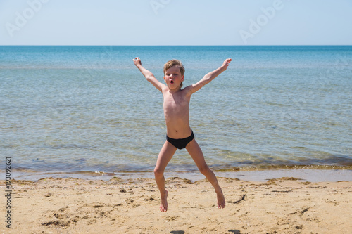 Foto Six-year-old boy in black speedo jumping into the sea and shouts.