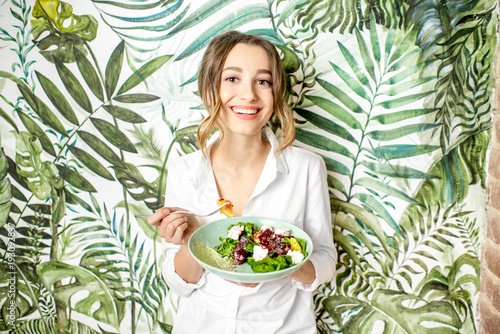 Fototapeta Portret młodej kobiety ze zdrowym jedzeniem na pięknej ścianie z zielonymi roślinami rysunki na tle