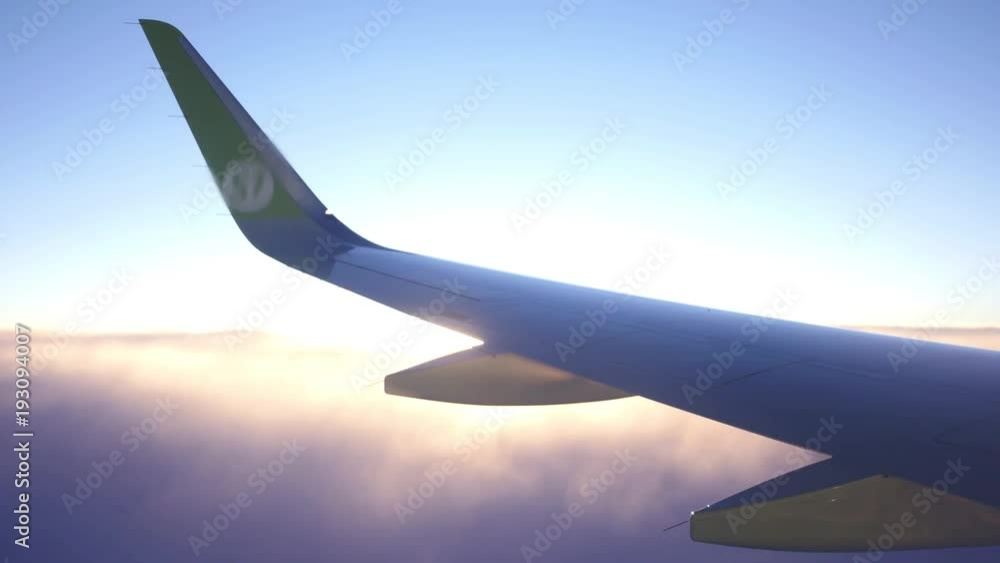 The wing of the plane from the window is high in the sky above the clouds at dawn. 4k, 3840x2160. HD The wing of the plane from the window is high in the sky above the clouds at dawn. 4k, 3840x2160. HD