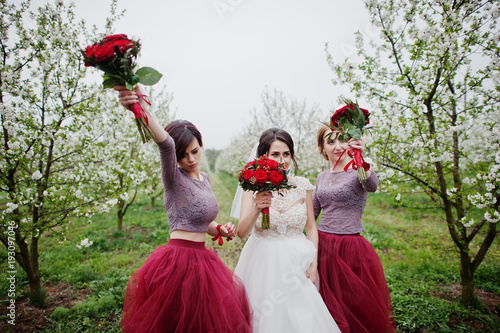 Fabulous bride and her bridesmaids holding bouquets and feeling elated in the garden on wedding day.