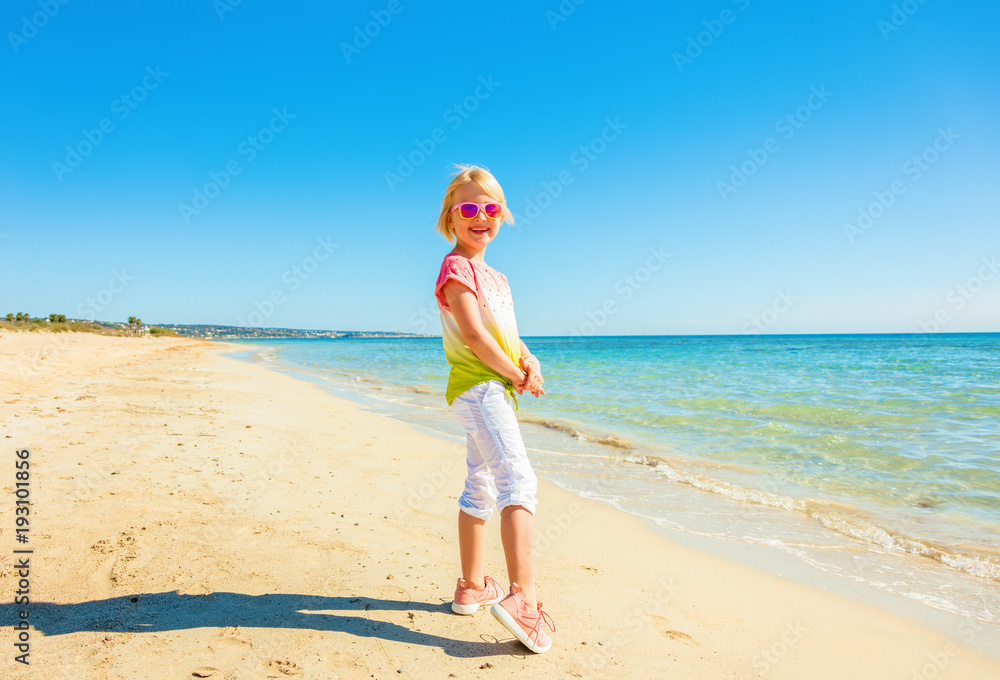 smiling modern child standing in colorful shirt on beach
