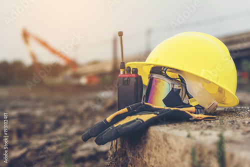 Yellow helmets, gloves, radio communication and safety glasses placed on the cement floor are the background of the construction of blurred buildings.