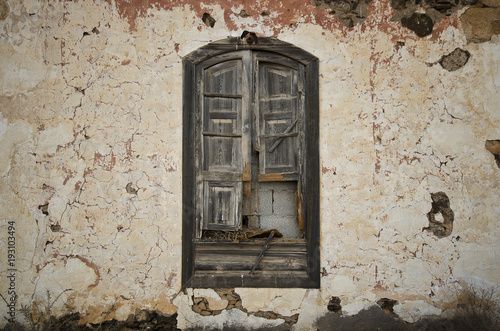 Alte Mauer mit Fenster und verwitterten Fensterläden aus Holz.
