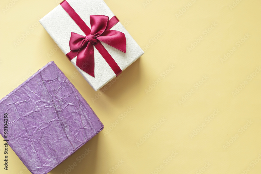 Gift boxes on yellow pastel background with copy space. Top view flat lay design. Violet square box and box with dark pink ribbon. Gifts for Women's Day, Mother's Day, birthday etc Gift boxes on yellow pastel background with copy space. Top view flat lay design. Violet square box and box with dark pink ribbon. Gifts for Women's Day, Mother's Day, birthday etc