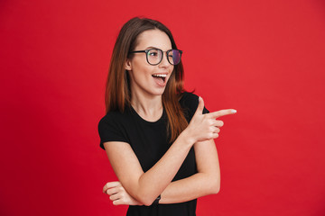 Image of cheerful woman with long brown hair winking and showing index finger aside meaning hey you, isolated over red background