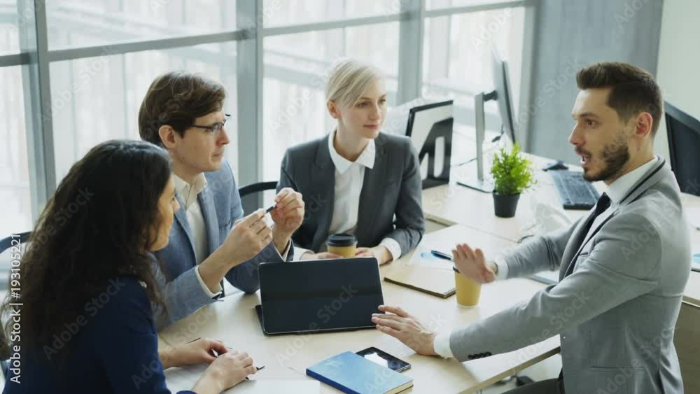 Businessman discussing future business project with male and female colleagues sitting at the table in modern office Businessman discussing future business project with male and female colleagues sitting at the table in modern office