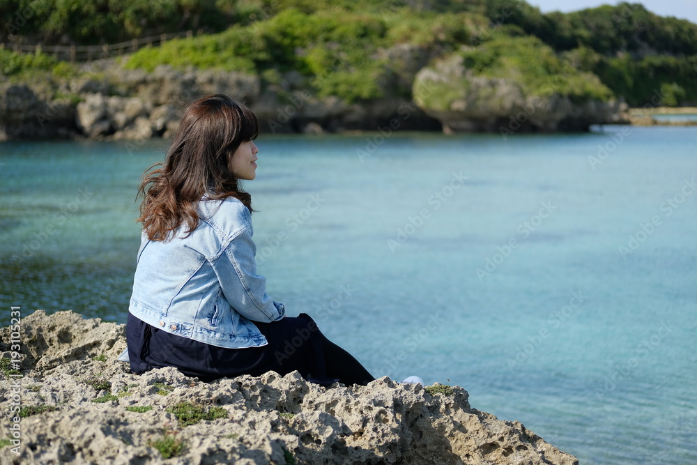 海辺の岩場に座る女性