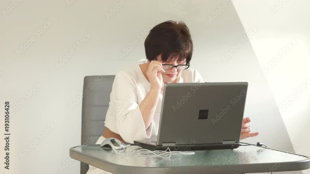 Woman in the office behind a computer screen. Business style clothing, glasses for working with a computer. Looks over the glasses, smiling Woman in the office behind a computer screen. Business style clothing, glasses for working with a computer. Looks over the glasses, smiling