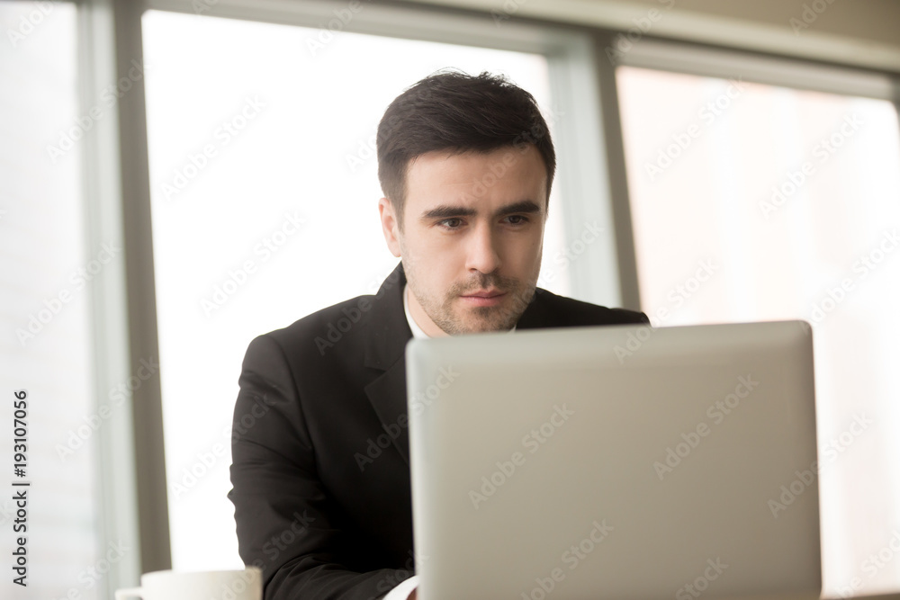 Portrait of handsome millennial businessman working on laptop, successful CEO reading business news online, using computer in office. Trader or broker monitoring exchange rate fluctuations in Internet Portrait of handsome millennial businessman working on laptop, successful CEO reading business news online, using computer in office. Trader or broker monitoring exchange rate fluctuations in Internet