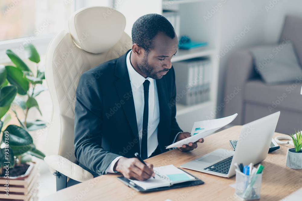 Hardworking financier sitting at desktop in workstation, workplace, watching, looking at documents, report, making notes in his notebook Hardworking financier sitting at desktop in workstation, workplace, watching, looking at documents, report, making notes in his notebook