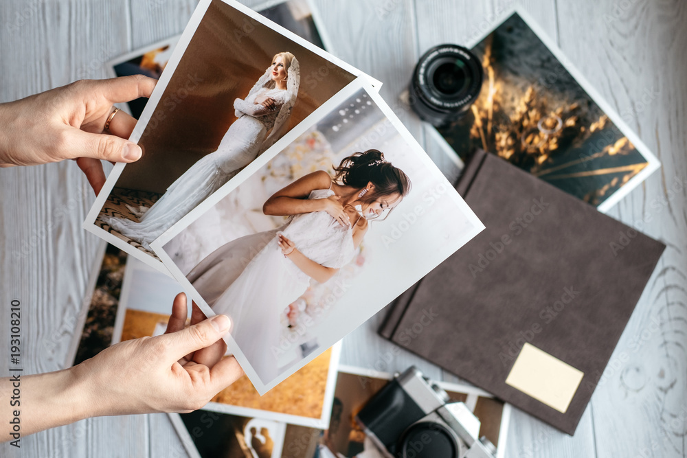 Printed wedding photos with the bride and groom, a vintage black camera, photoalbum and woman hands with two photos - obrazy, fototapety, plakaty 