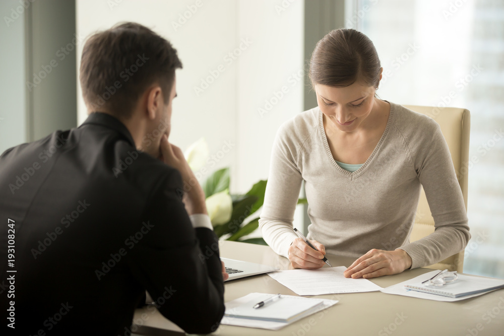 Satisfied with loan terms woman singing contract when sitting at desk in front of male bank employee at office. Millennial female applicant accepting employers offer and putting signature in agreement Satisfied with loan terms woman singing contract when sitting at desk in front of male bank employee at office. Millennial female applicant accepting employers offer and putting signature in agreement