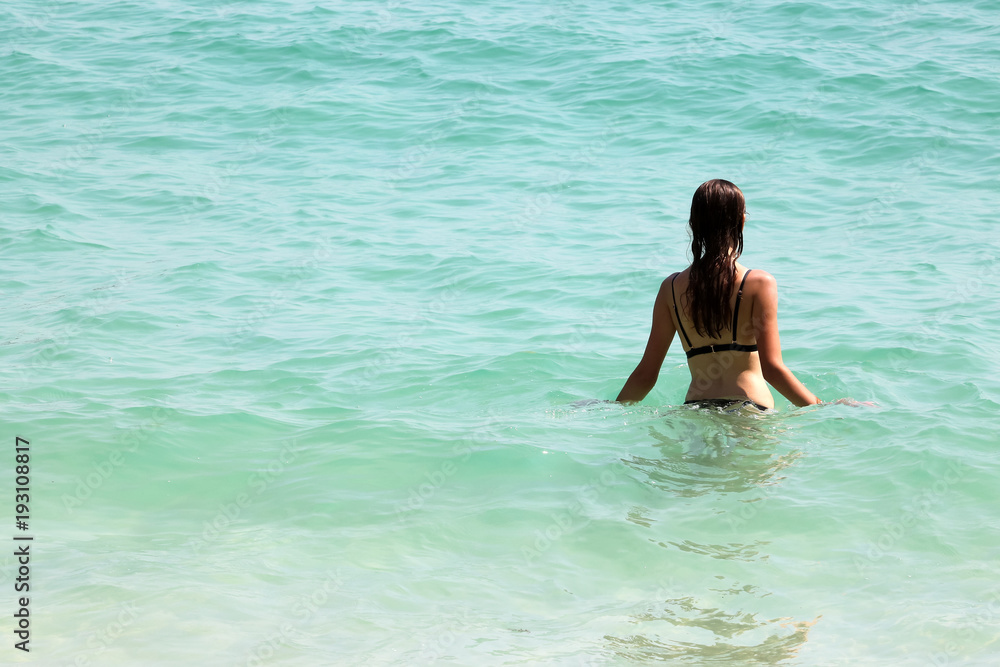 Back view of tourist girl in bikini walking into the sea on the beach