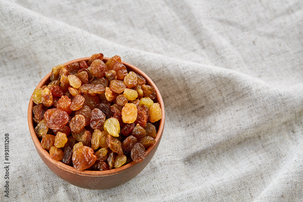 Ceramic bowl with golden raisins on light tablecloth, close-up, selective focus Ceramic bowl with golden raisins on light tablecloth, close-up, selective focus