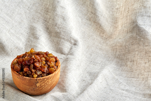 Wooden bowl with golden raisins on light tablecloth, close-up, selective focus photo