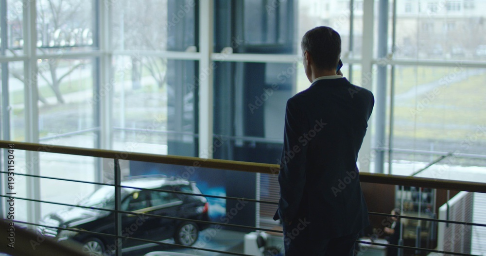 Adult businessman in suit standing in showroom and having mobile phone conversation. Adult businessman in suit standing in showroom and having mobile phone conversation.