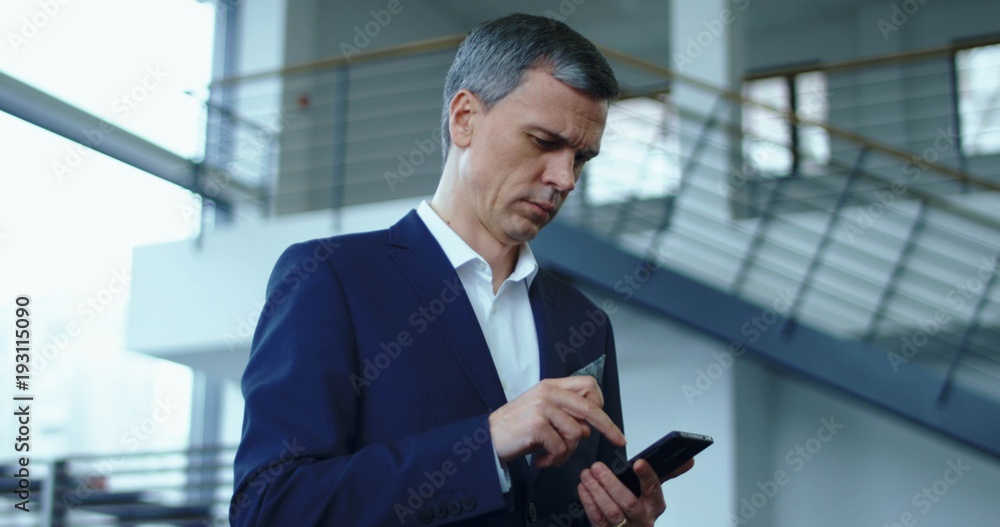 Handsome adult businessman in blue suit standing and browsing smartphone.