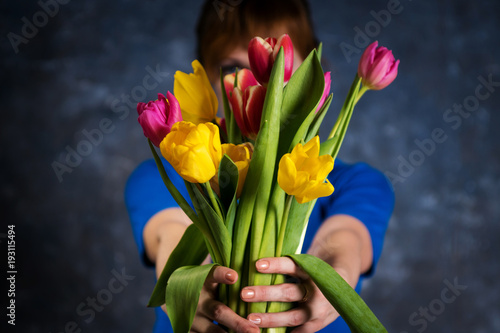 the girl in a blue dress holds in her arms a bouquet of yellow-red tulips, covering her face