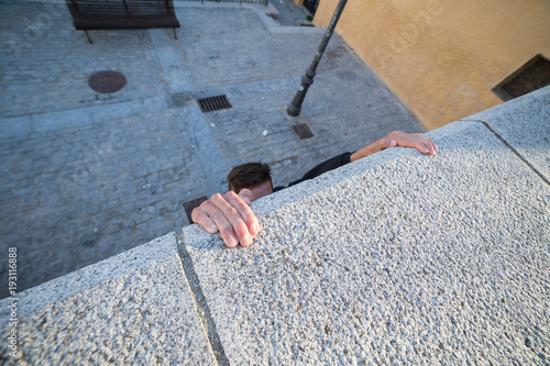 Young man hanging on wall on hands and trying to climb up while doing parkour.  